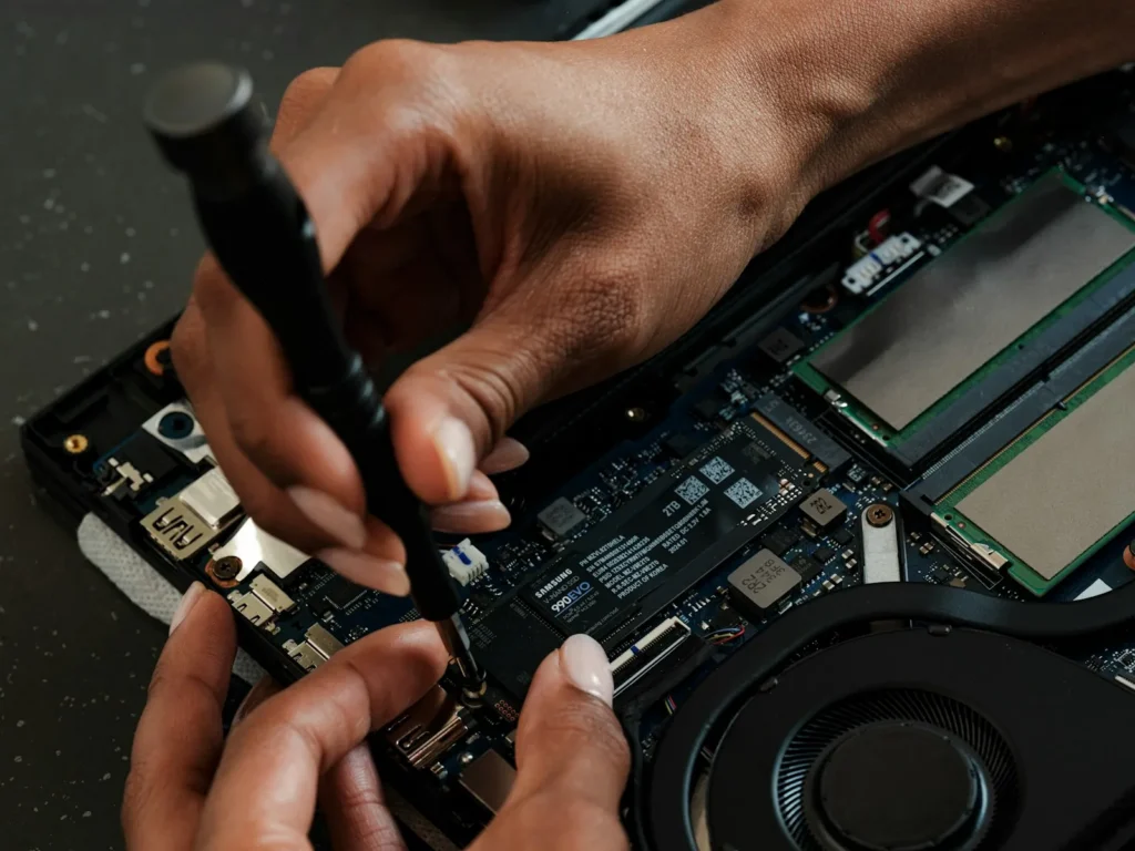 Technician’s hands repairing the inside of a laptop with a screwdriver
